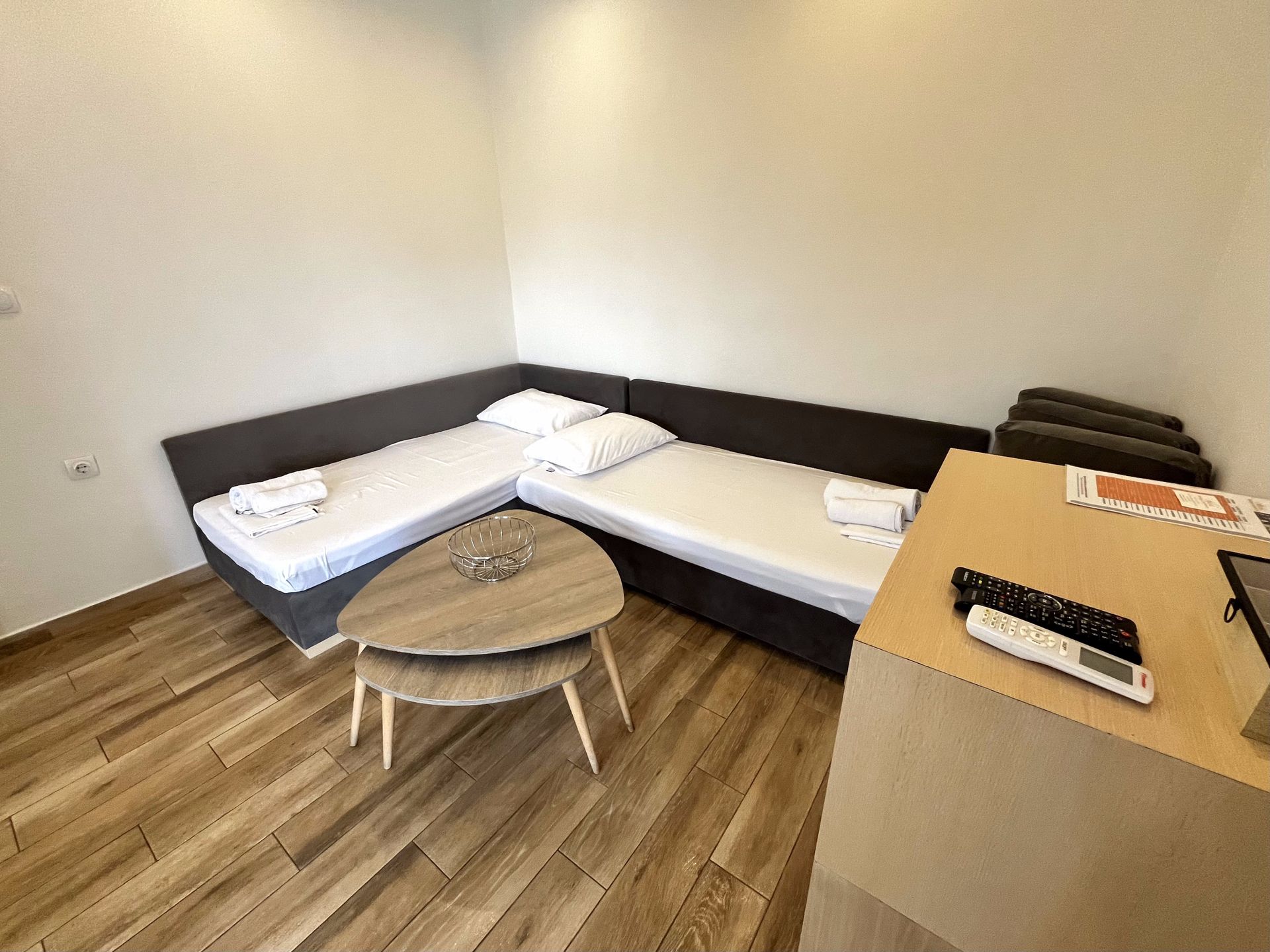 L-shaped bed in a room with a wooden floor, small table, and a desk.