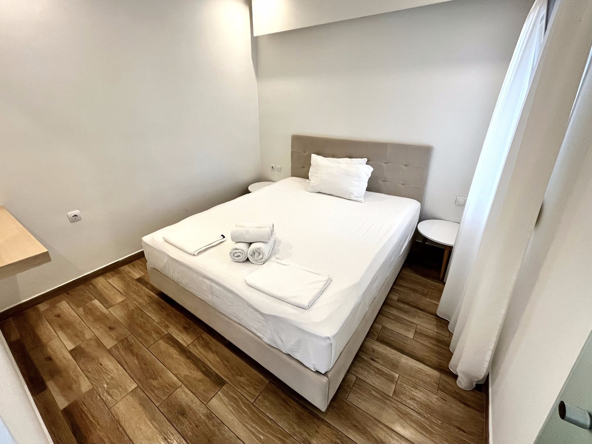Bedroom with a bed, white linens, towels, a bedside table, and wood-look flooring.