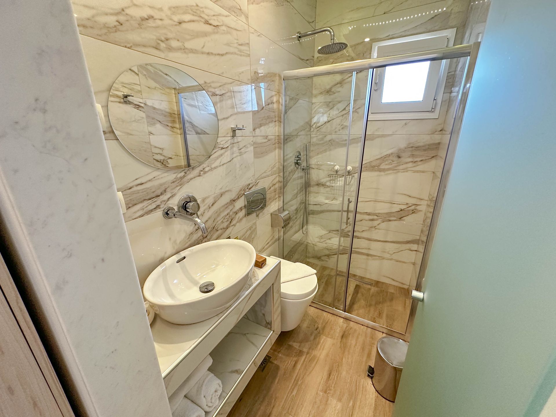 Modern bathroom with marble-look walls, oval sink, glass shower, and toilet.