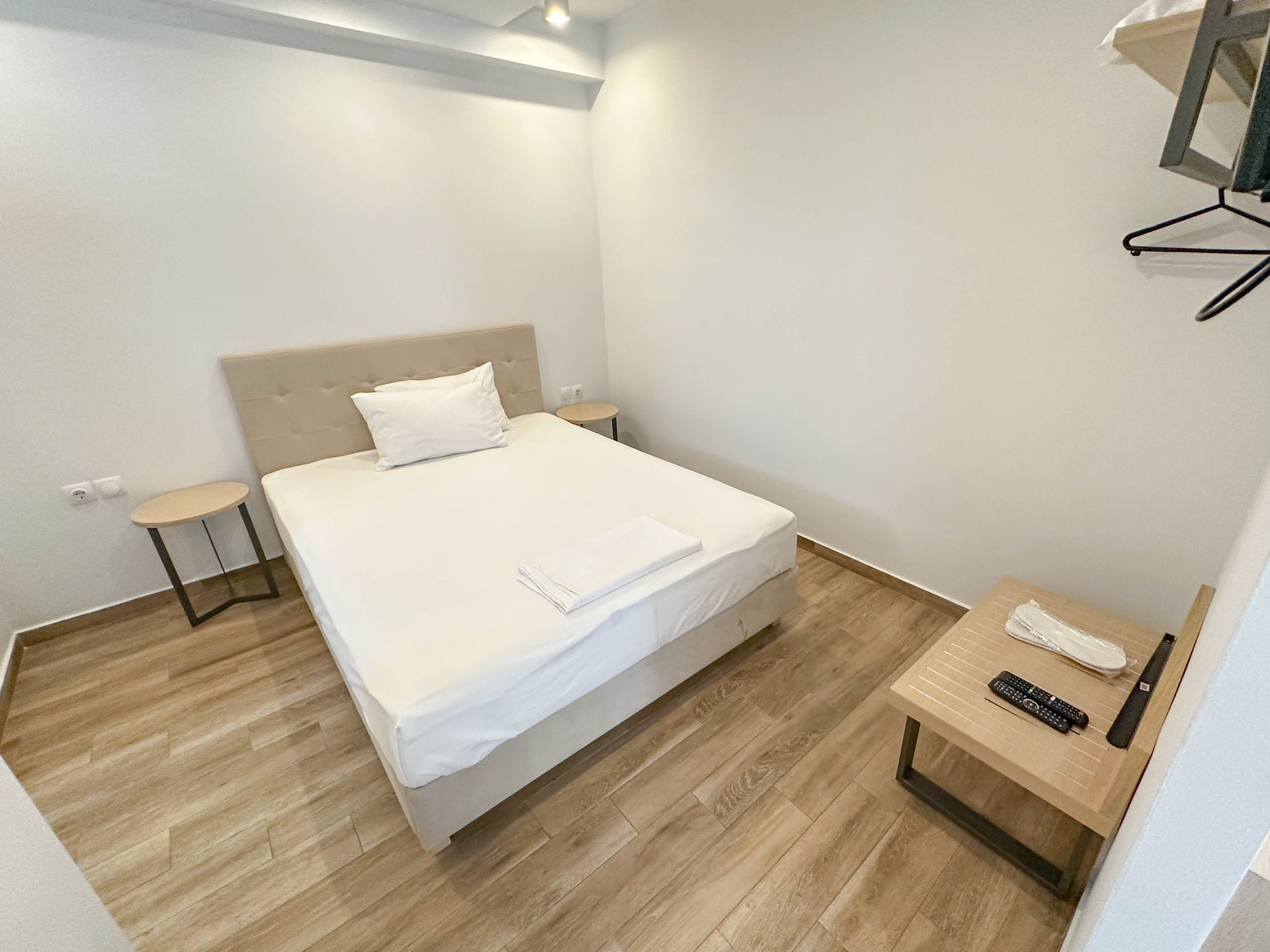 Bedroom with white walls, a bed, two small tables, and a wooden floor.