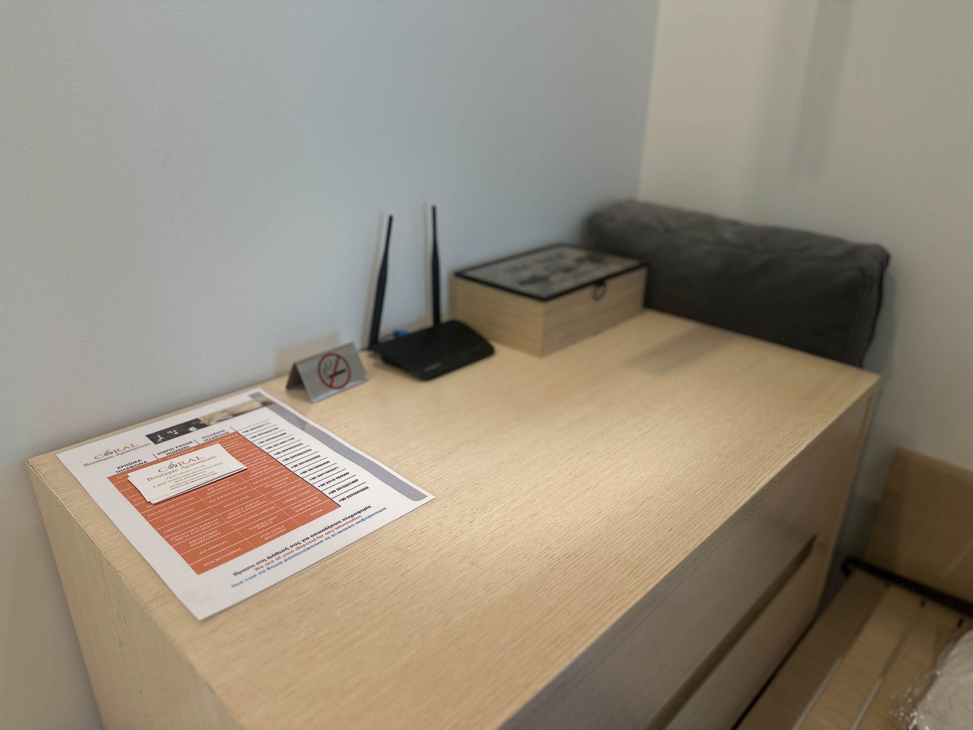 A light wood dresser with a router, box, sign, and pillow. Located against a white wall in a room.