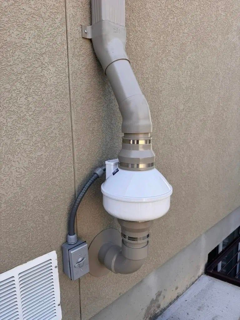Exterior wall vent pipe with a white inline filter housing and attached gray ducting.