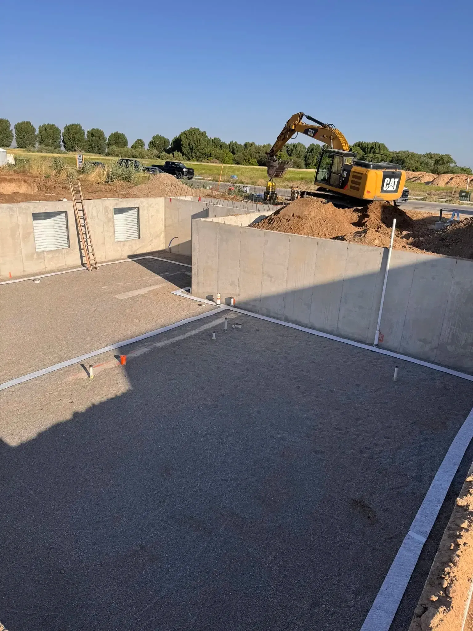 Construction site with excavator behind concrete retaining walls and gravel foreground