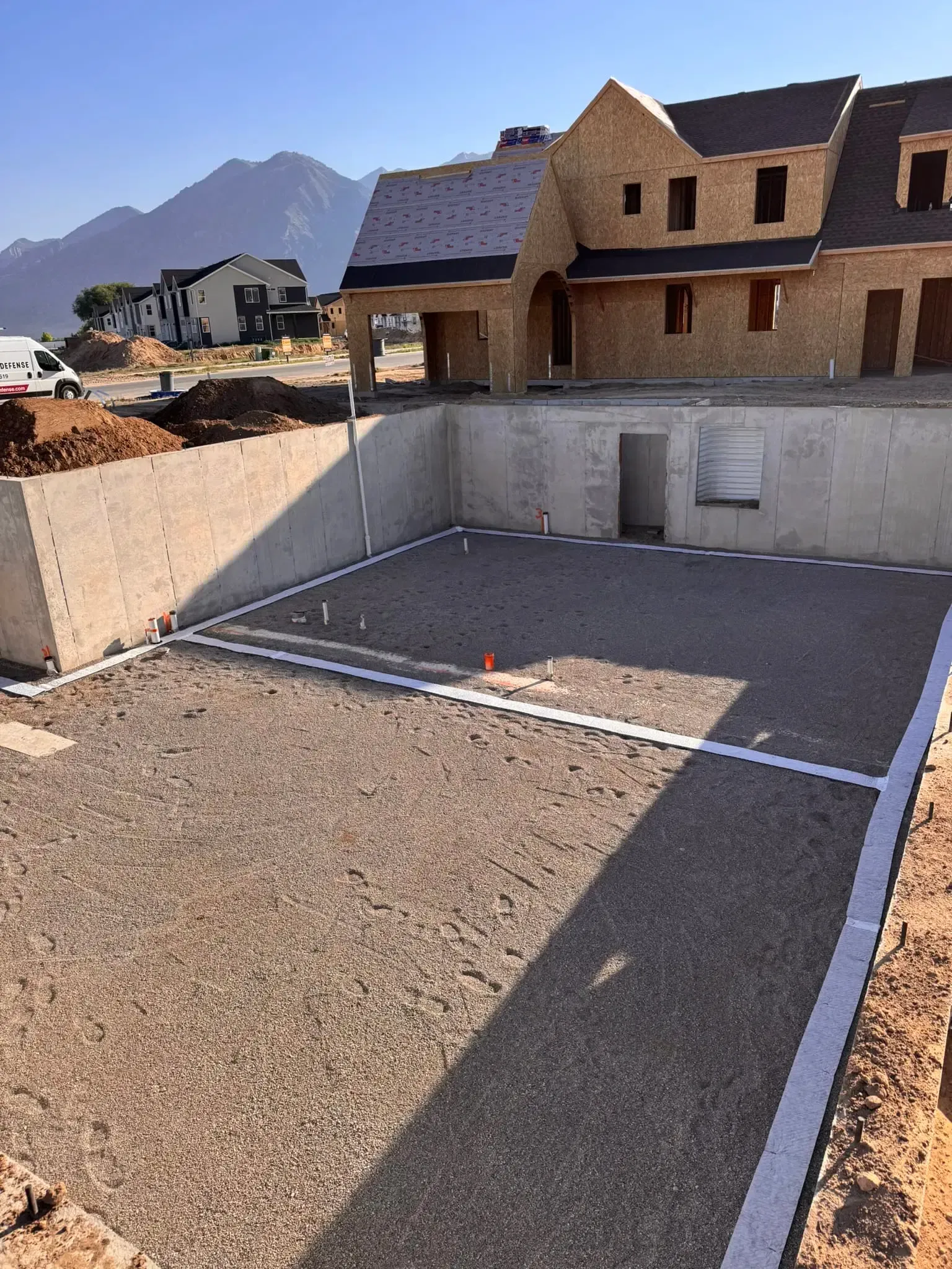 Empty concrete basement foundation under construction beside a house, with gravel and mountains in the background