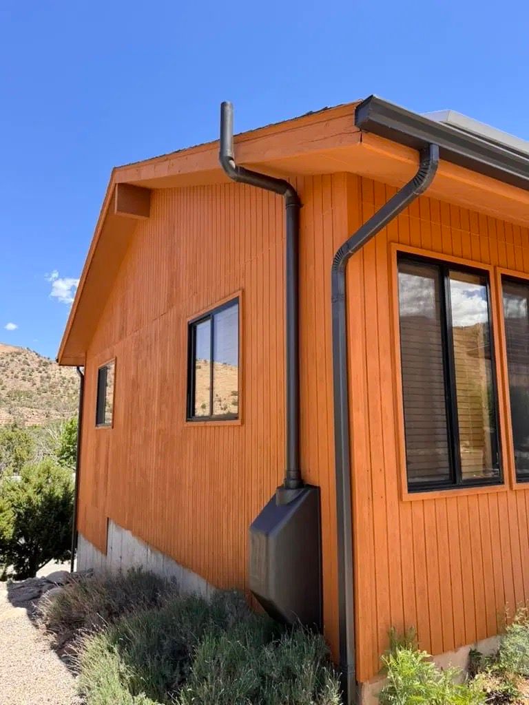 Orange wooden house exterior with black gutters and a large window under a blue sky
