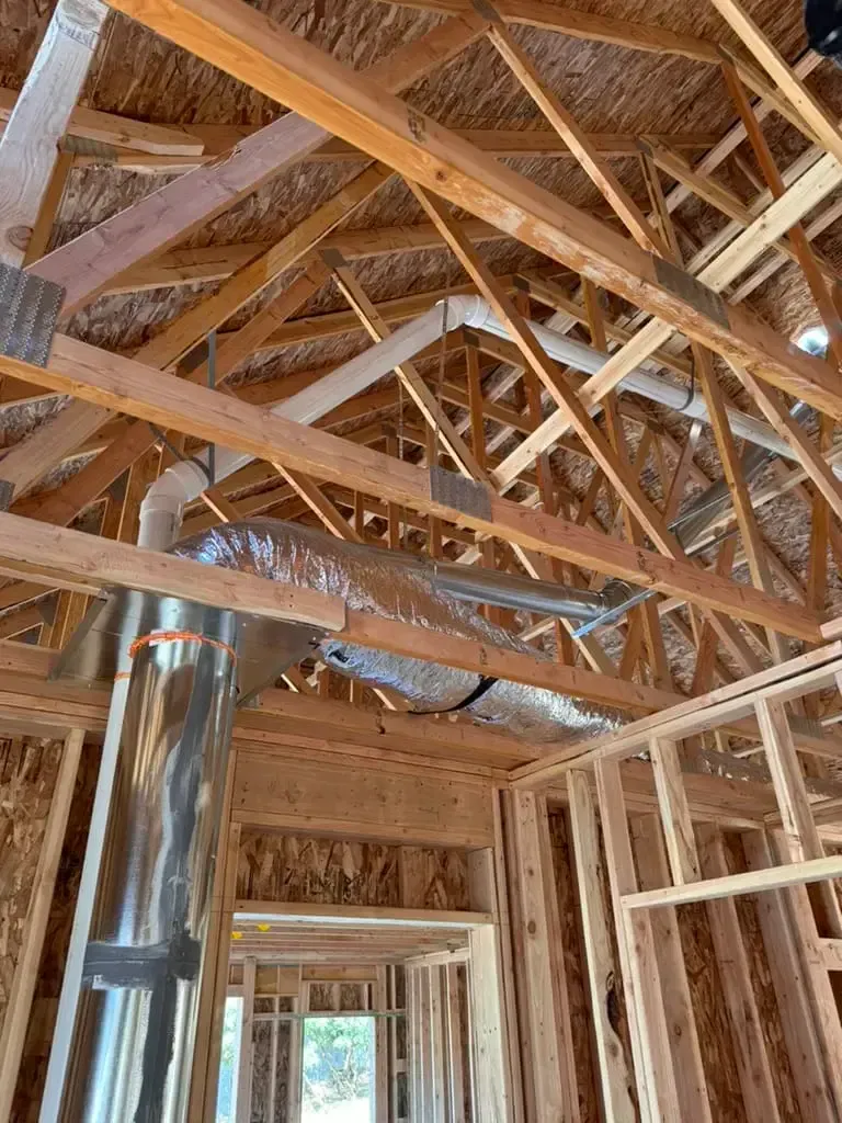 Exposed wooden roof framing and rafters inside a house under construction, with a doorway below.