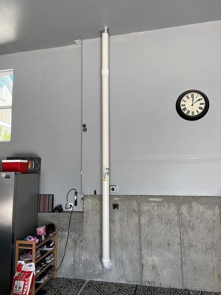 Indoor wall with a vertical white pipe and a clock, above a concrete lower wall in a garage-like room