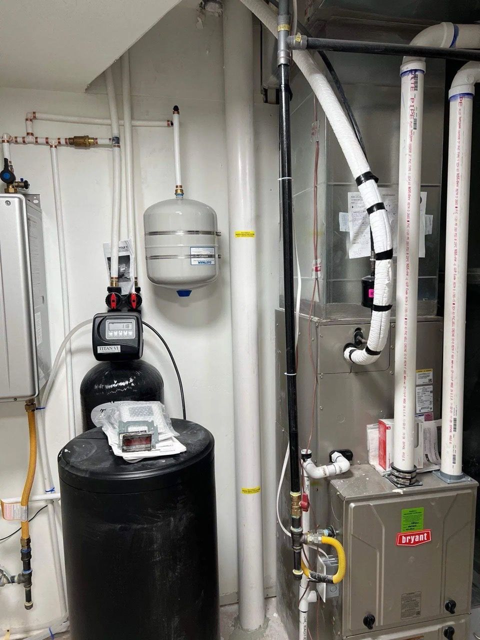 Basement utility room with water softener tanks, pipes, and a water heater.
