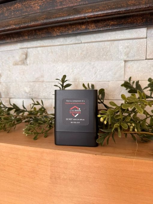 Black box candle on wooden shelf with greenery and stone wall backdrop