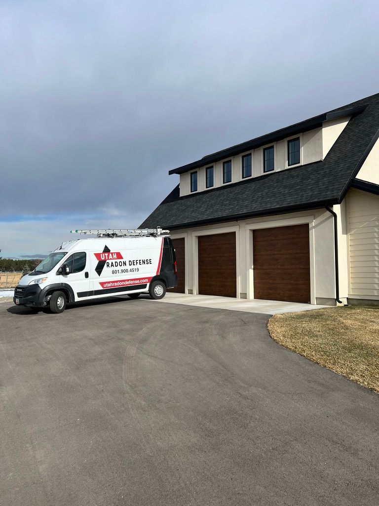 White service van parked outside a beige house with three brown garage doors under a cloudy sky