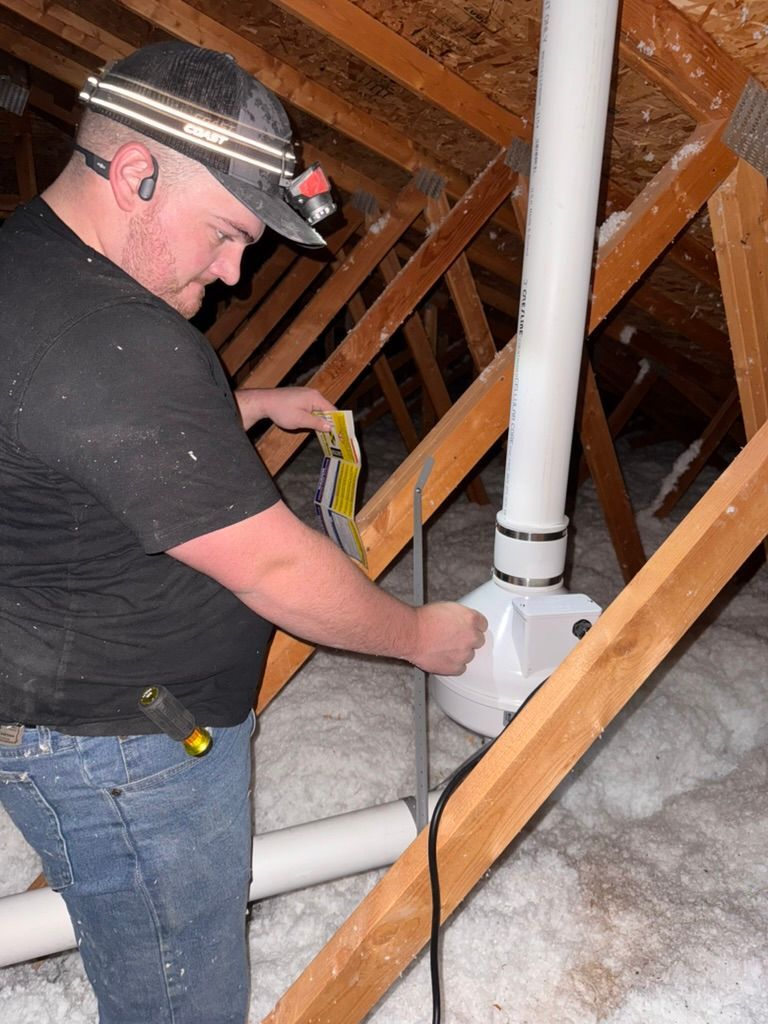 Man installing white PVC pipe in an attic with exposed rafters and insulation.