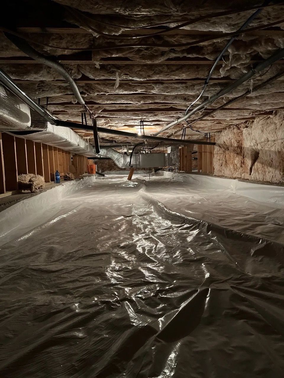 Flooded basement with a plastic sheet covering the floor and exposed wooden beams overhead