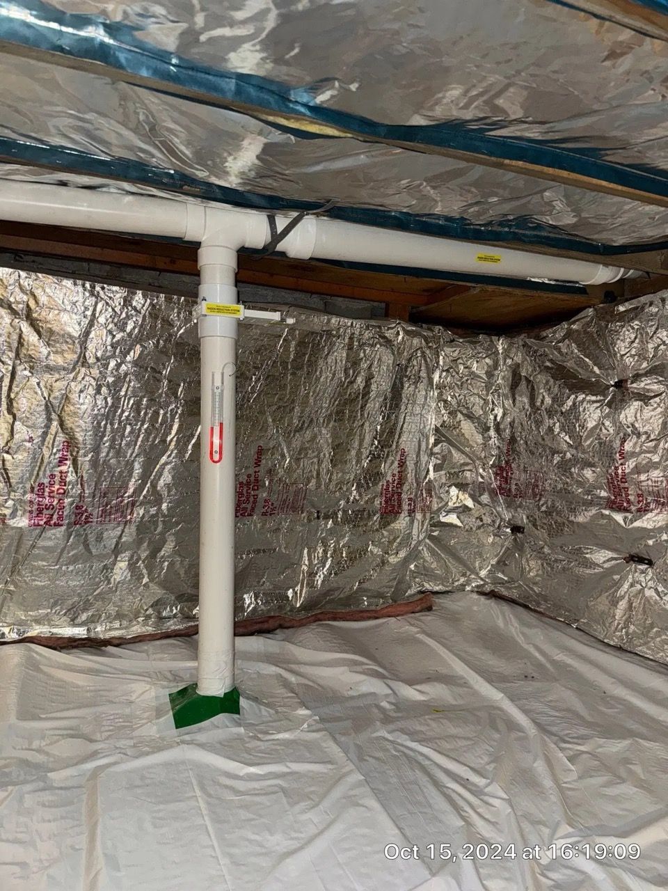 Insulated crawlspace with foil-lined walls and ceiling, white support post, and plastic sheeting on the floor