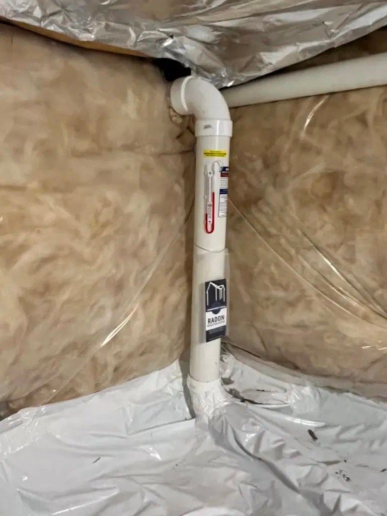White PVC pipe and elbow joint in an insulated attic space, wrapped in foil insulation.
