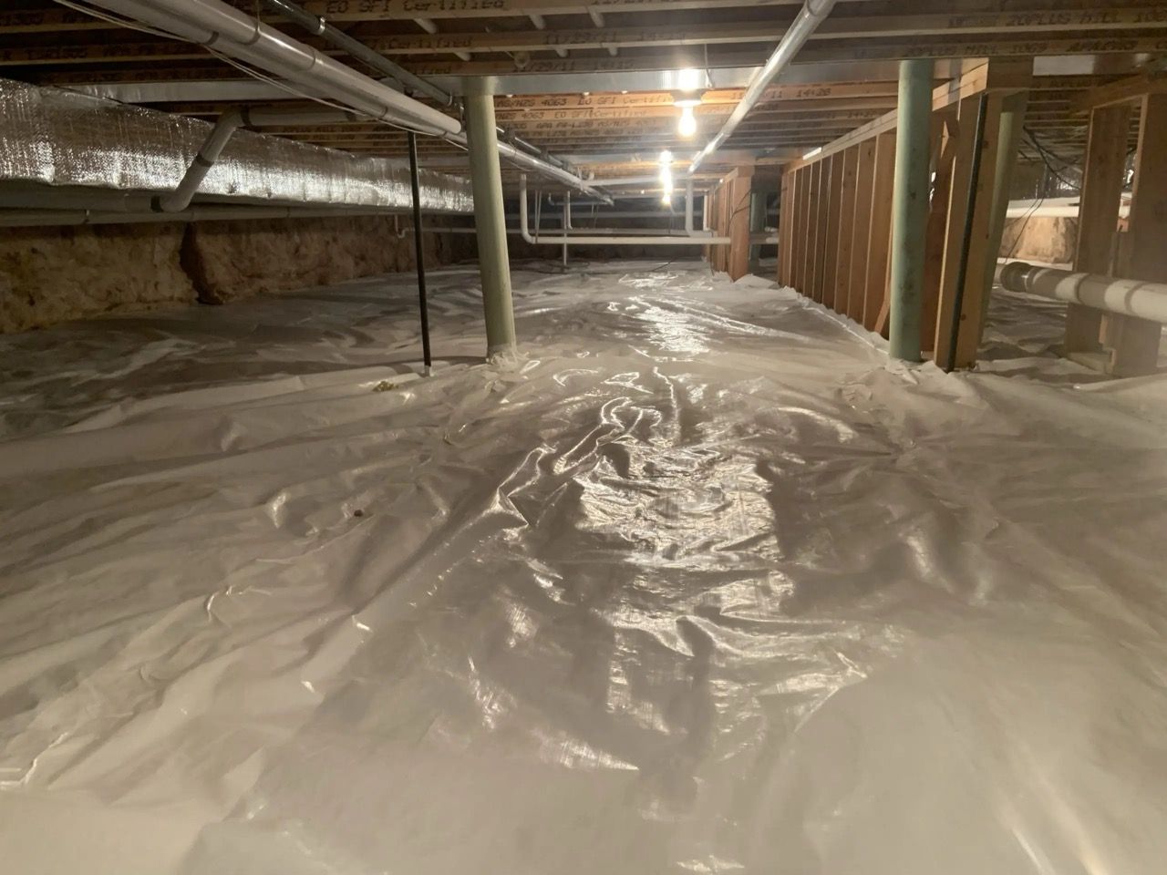 Partially finished basement with plastic vapor barrier on the floor and exposed beams overhead