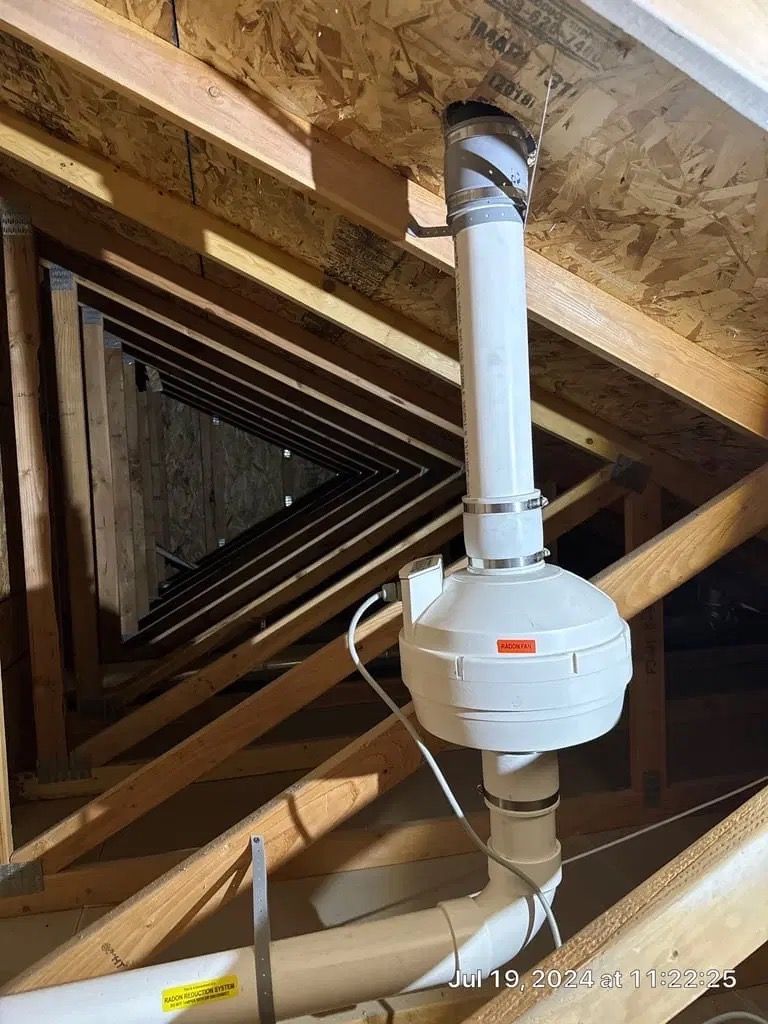 Basement attic space with white HVAC duct and vent pipe under exposed wooden framing.