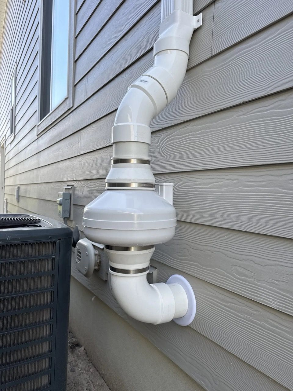 White roof vent pipe on beige house siding beside an outdoor air conditioner unit