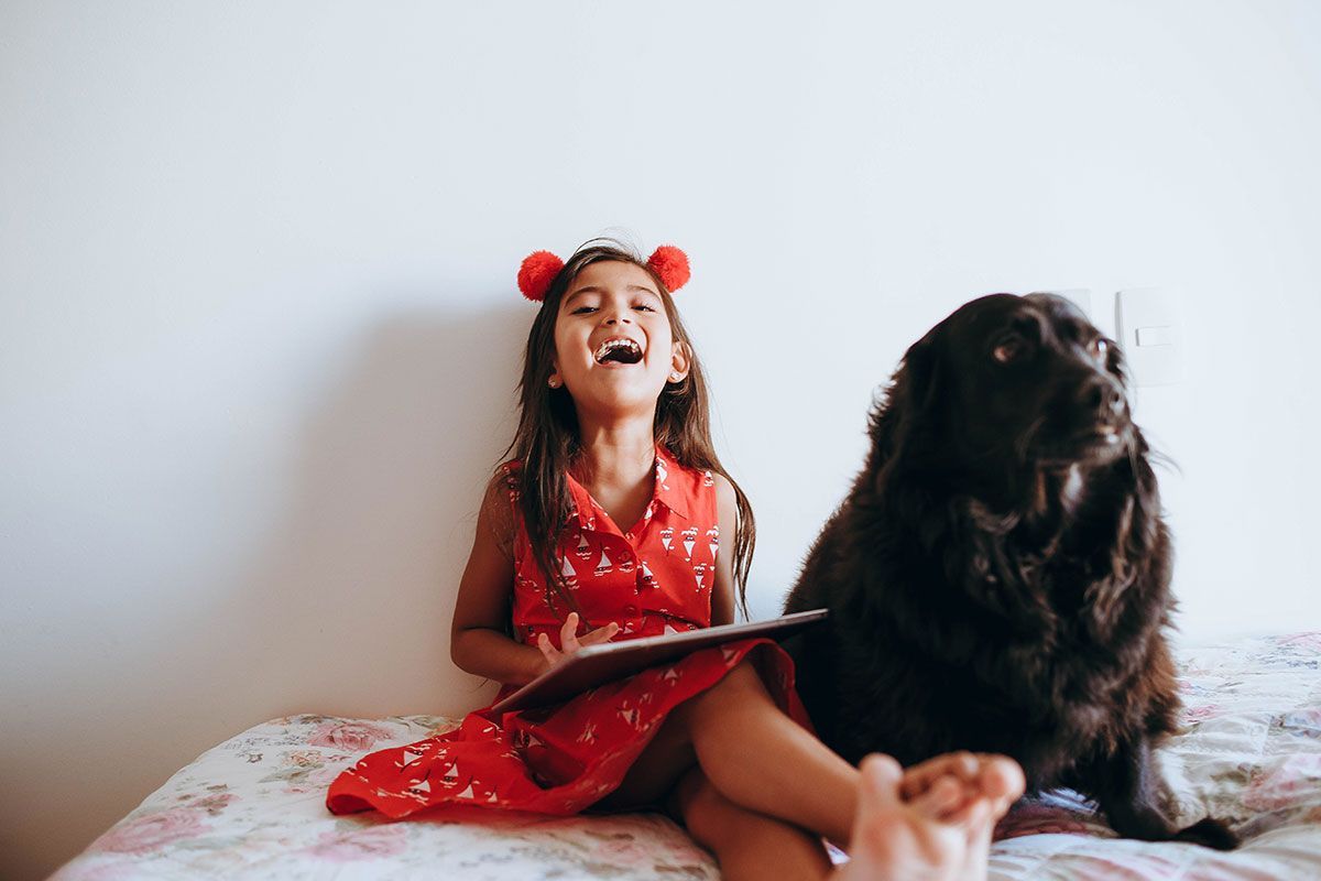 Girl in red dress reading a book to her dog and laughing