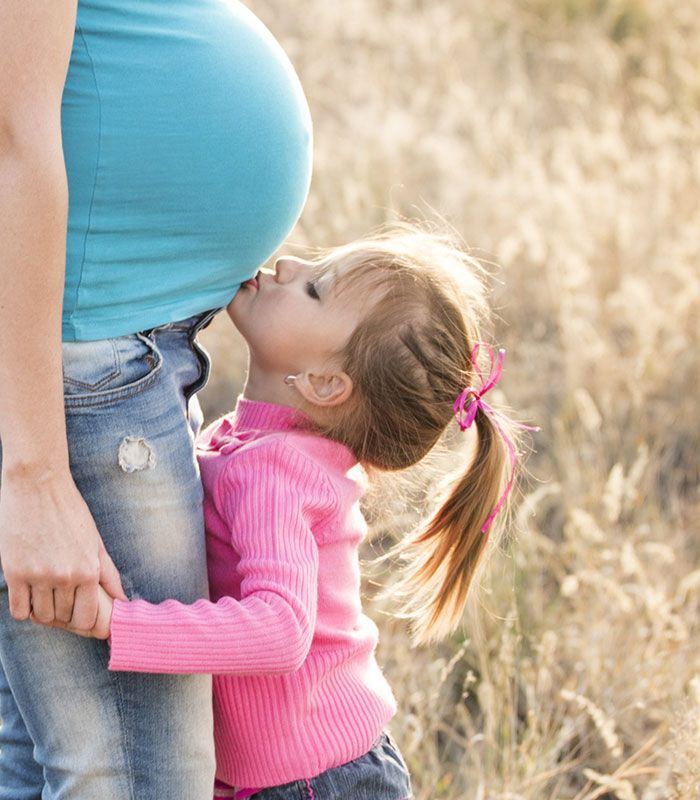 Little girl kissing the belly of her pregnant mom