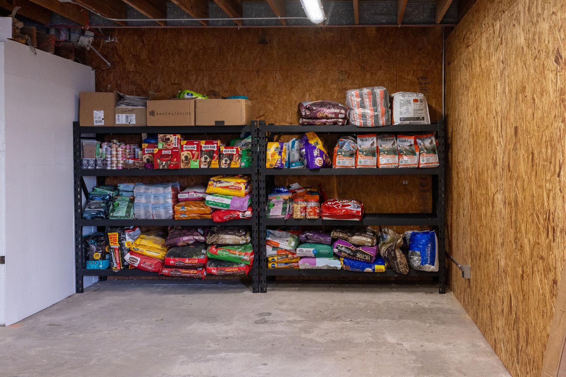 Storage shelves filled with pet food and supplies in a basement or storage room.