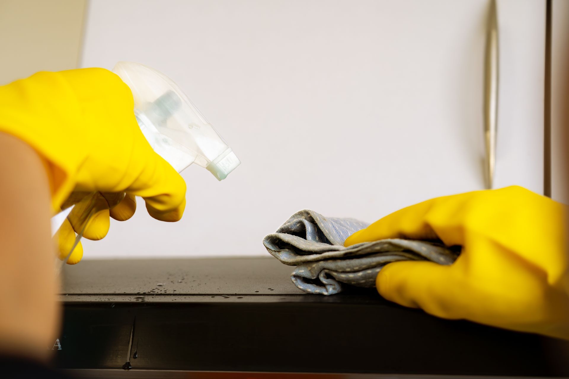 Gloved hands spraying cleaner and wiping a surface with a cloth during cleaning