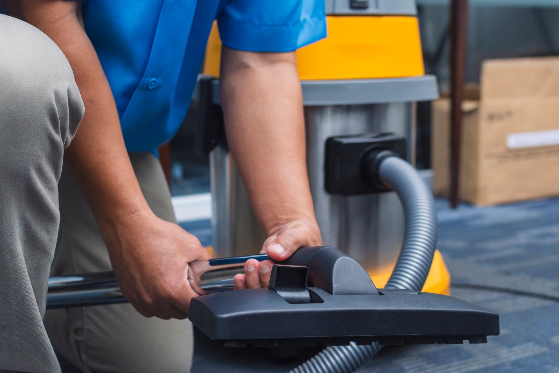 Person using a vacuum cleaner attachment on a floor in a workshop.