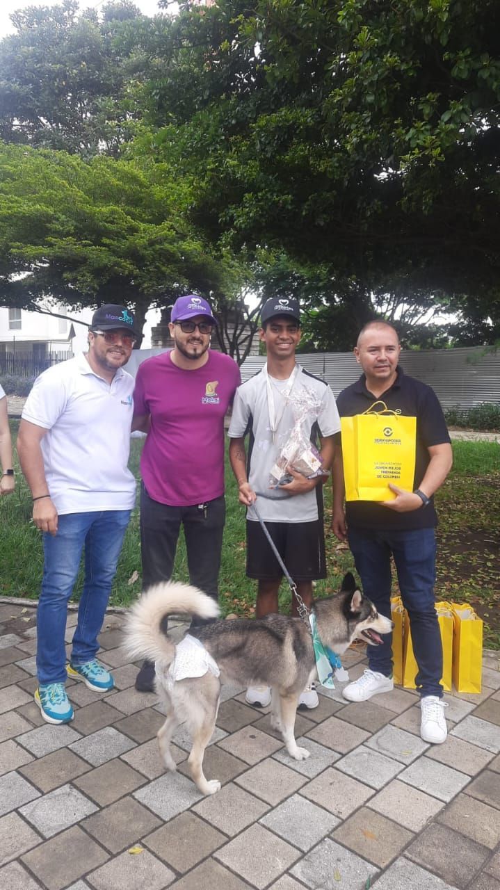 Cuatro personas y un perro posando con premios al aire libre; el perro tiene una correa.
