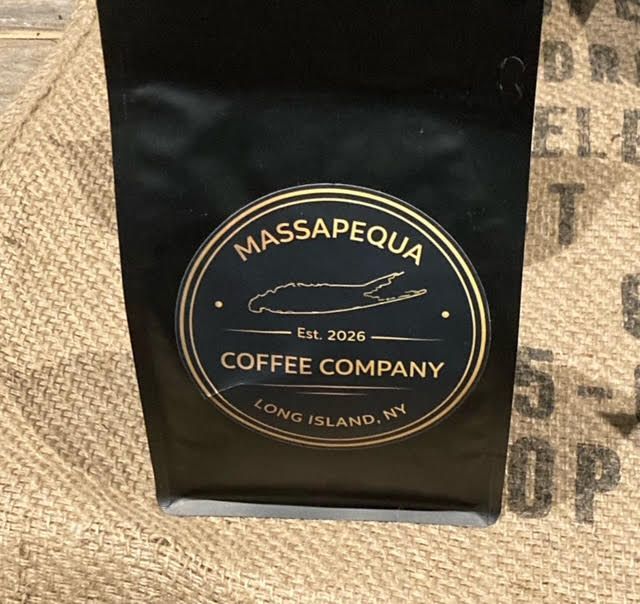 A person pours dark coffee from a glass carafe into a row of three small white bowls on a dark wooden table.