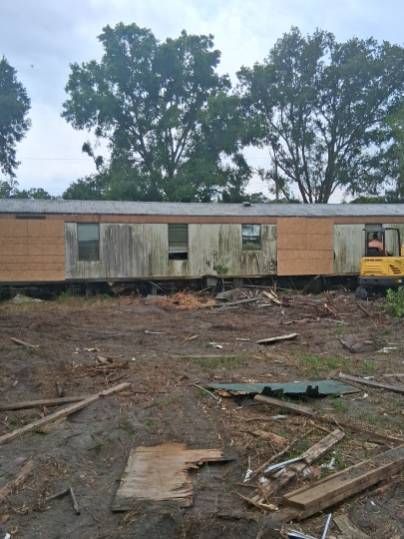 Derailed train car on muddy ground with debris and trees in the background