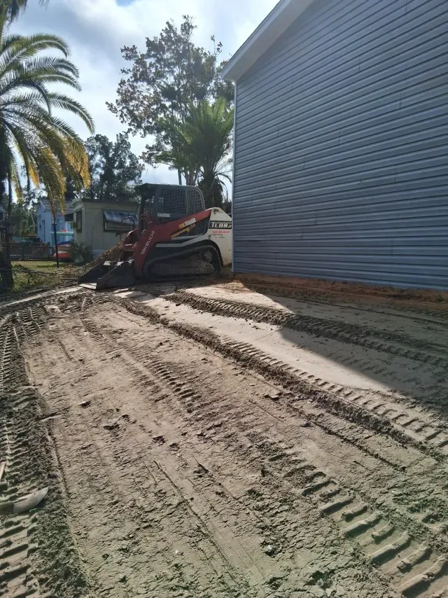 A red and white skid-steer loader sits beside the light blue, horizontal siding of a house under construction.