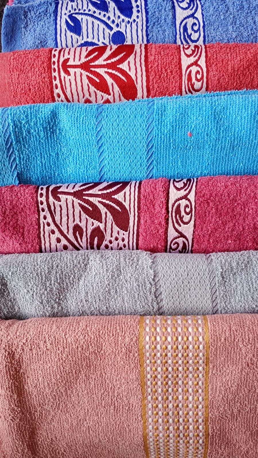 Toallas apiladas de colores con bandas decorativas. Los colores incluyen azul, rojo, turquesa, gris y rosa.