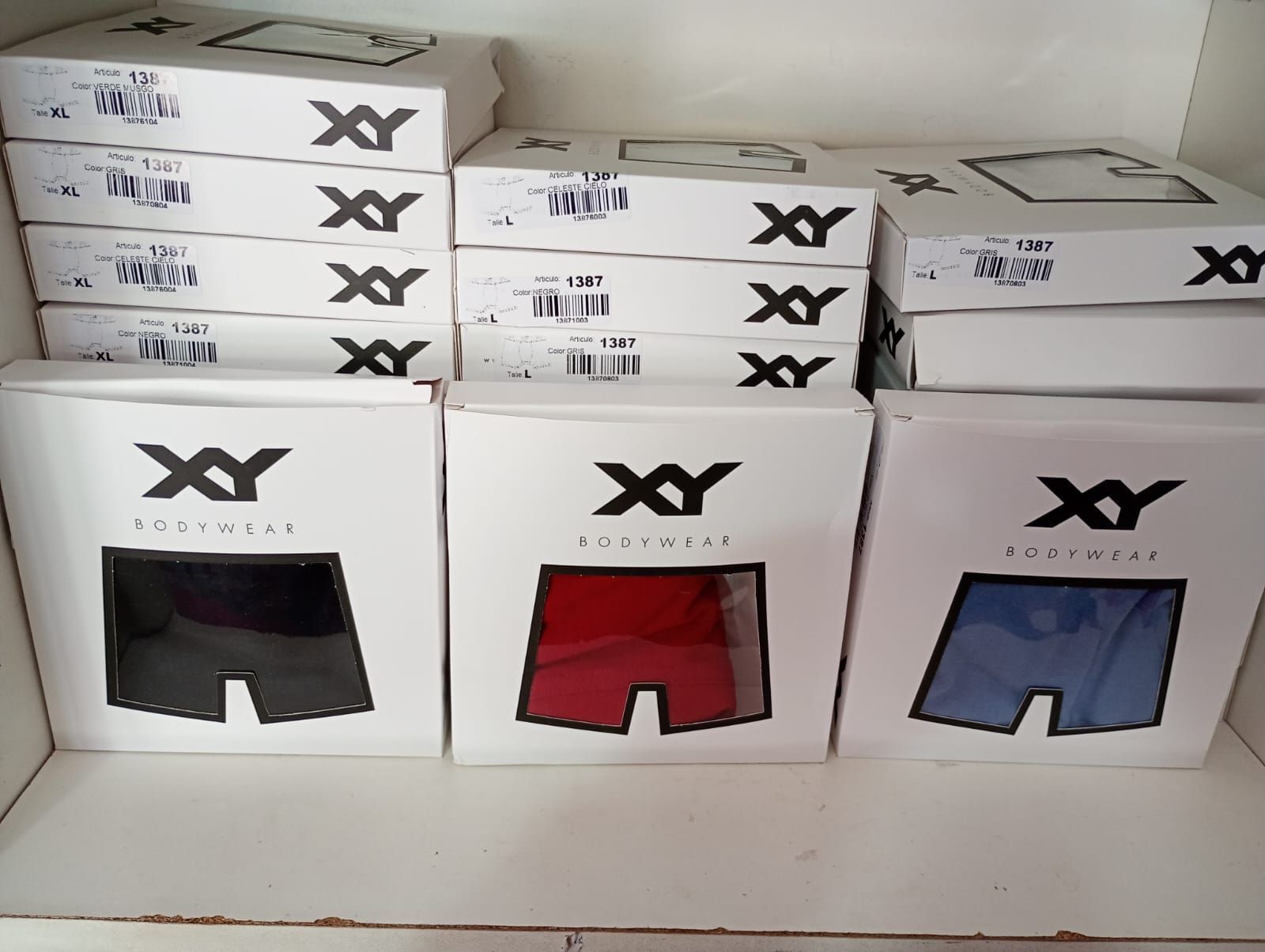 Cajas de ropa interior XY, en negro, rojo y azul, apiladas en un estante.