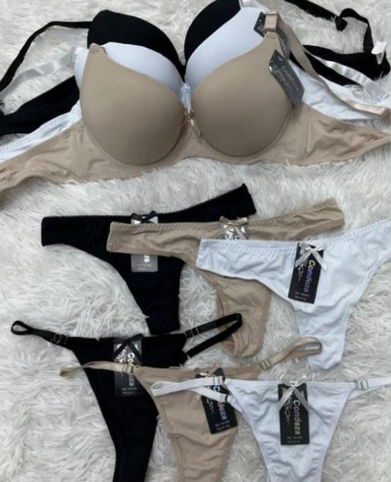 Sujetadores y tangas en colores negro, blanco y nude, dispuestos sobre una superficie blanca y esponjosa.