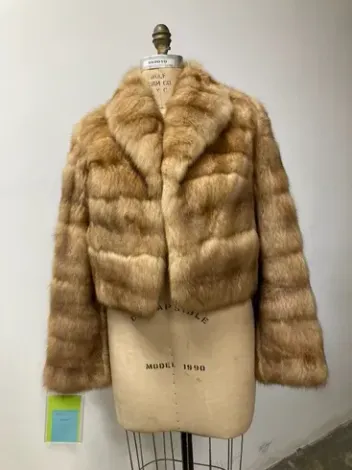 Cropped tan fur coat on a mannequin. Features a wide collar and horizontal fur pattern.