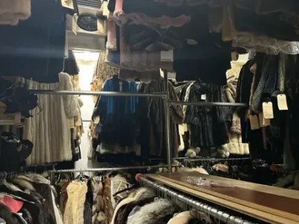 Clothes racks overflowing with coats and garments in a dimly lit storage space.