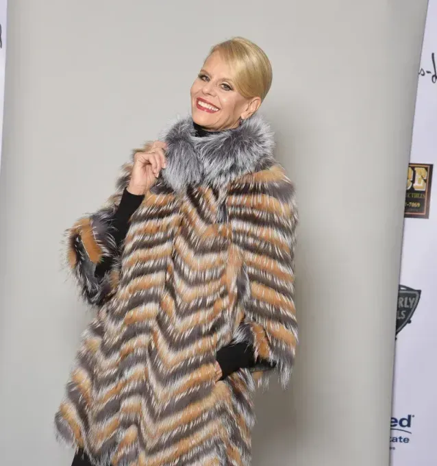 Woman in a colorful fur coat smiles, posing against a light background.