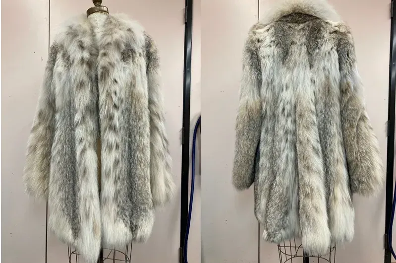 Front and back view of a long, light-colored fur coat with spotted pattern and a fur collar, displayed on a mannequin.
