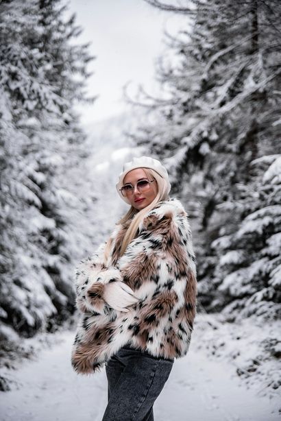 Woman in fur coat and hat poses in snowy forest.