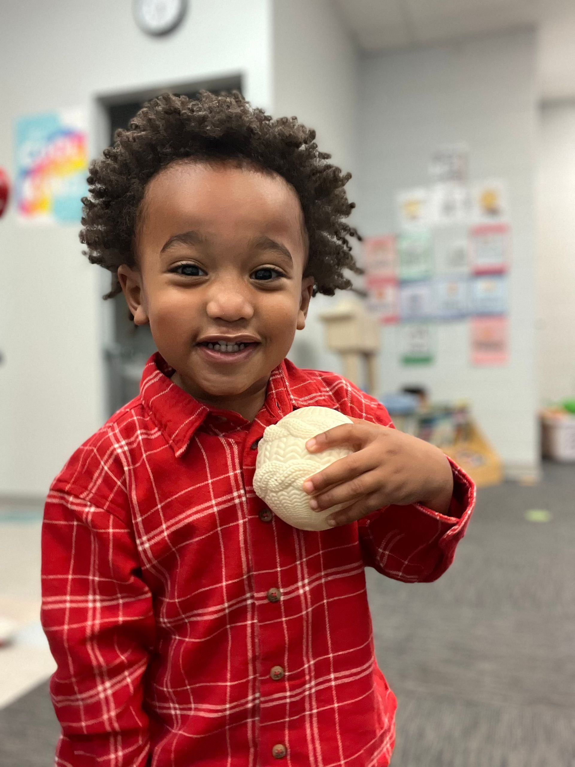 Preschool — Children Reading Books in Dyer, IN A young boy in a red shirt is sitting at a table with a blue chair - Dyer, IN - Bright Beginner's Academy