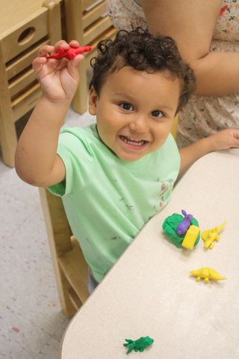 A little boy is sitting at a table holding a red toy dinosaur - Dyer, IN - Bright Beginner's Academy
