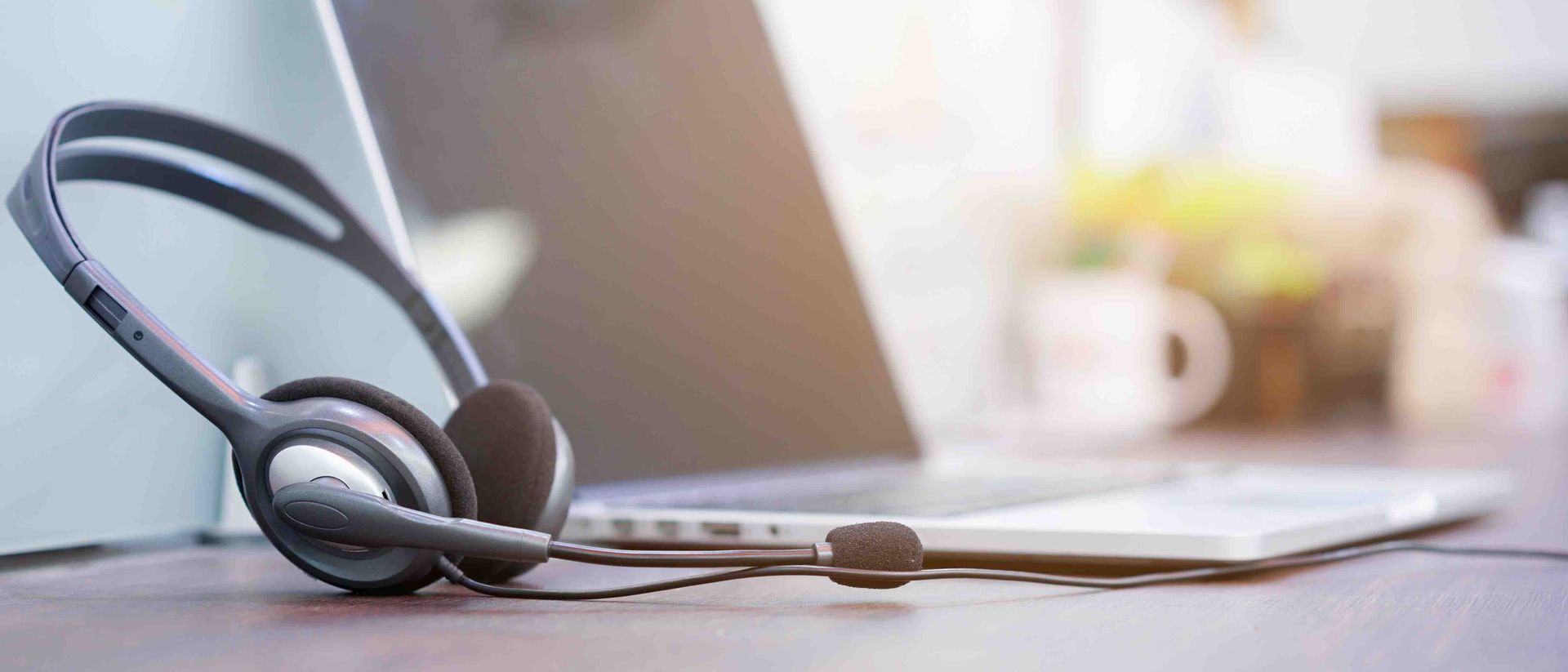 A pair of headphones is sitting on a desk next to a laptop computer.