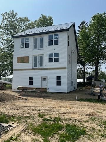 A large white house is being built in a dirt field.