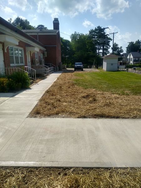 A concrete walkway leading to a house with a car parked in front of it.
