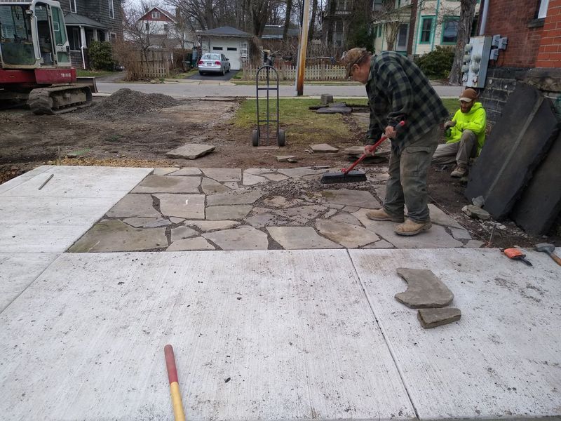 A man in a plaid shirt is working on a stone walkway