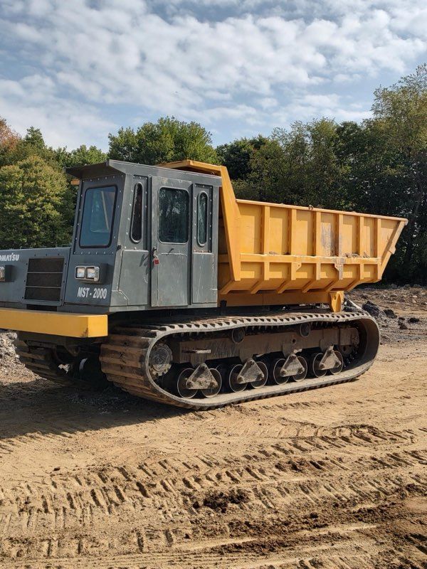 A yellow and gray dump truck is parked on a dirt road.