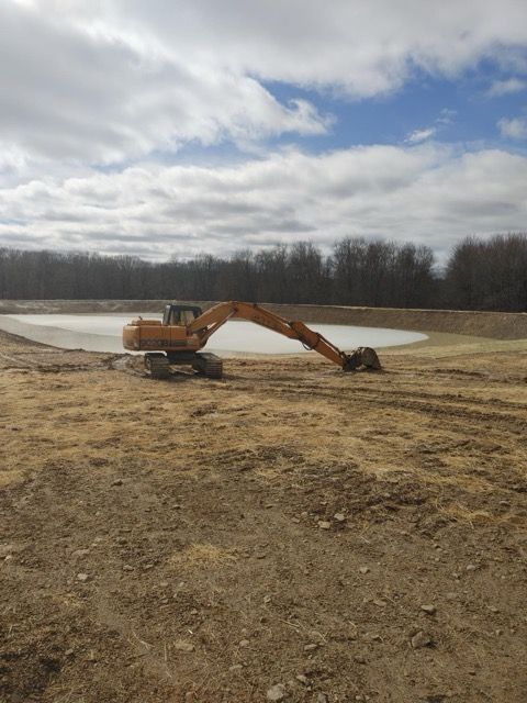 A large excavator is digging a pond in the middle of a dirt field.
