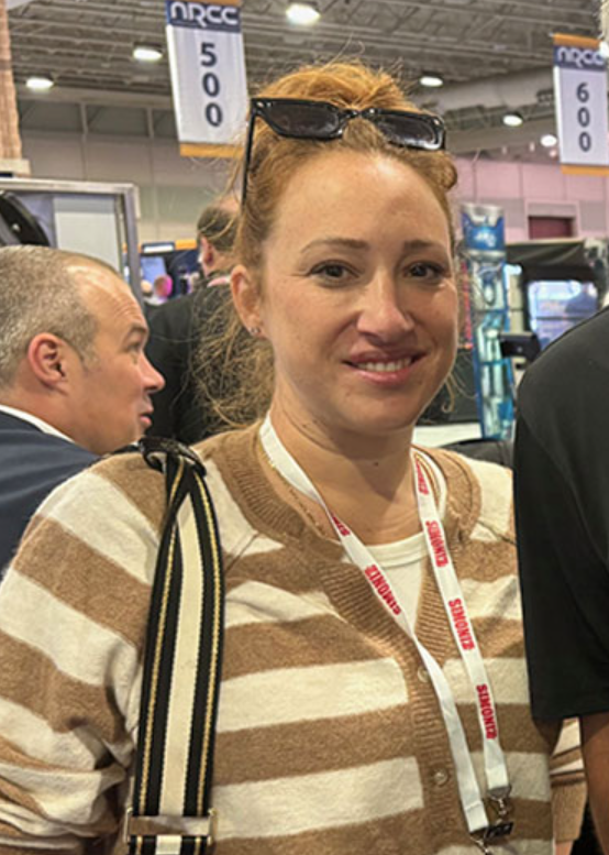 Woman in a striped sweater and lanyard smiling at an indoor event booth.