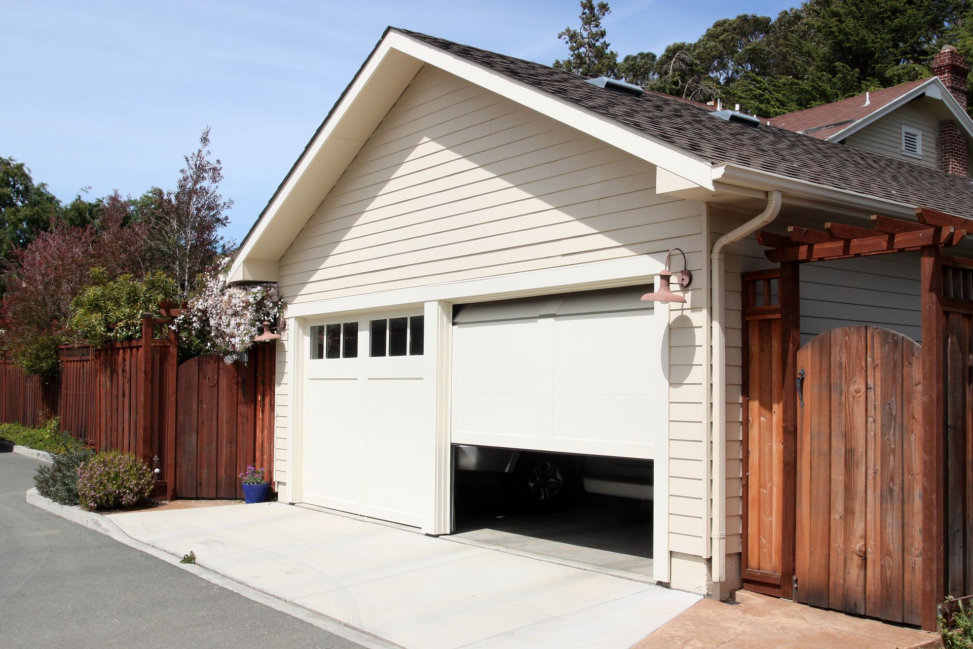 A two-car garage with white siding and one door partially open, viewed from the driveway next to a wooden fence.