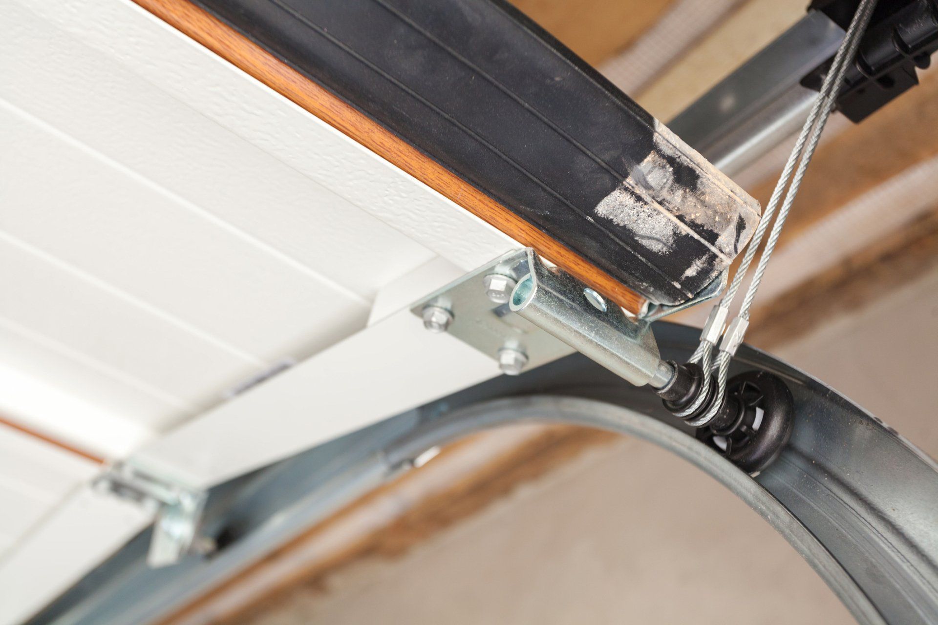 A close-up view of a garage door track with a metal roller and a steel lift cable attached to the door bracket.