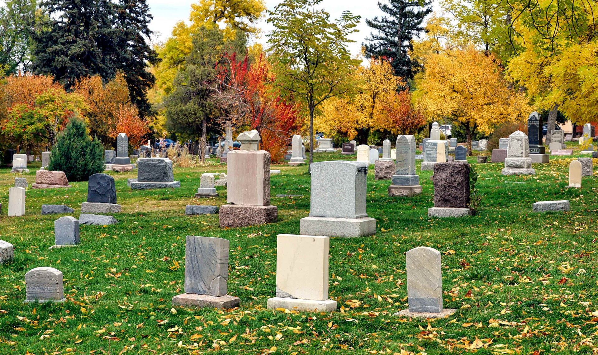 A cemetery with rows of headstones surrounded by colorful autumn trees on landscaped grounds